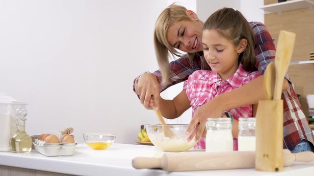 Dolly slider 4K footage of beautiful mother and young doughter cooking together at the kitchen. They are preparing dough for bake