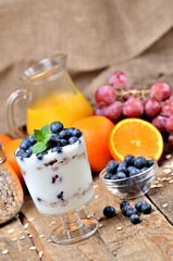 Greek yoghurt with oatmeal, fresh blueberries and mint leaves and orange and grapes in background vertical photo