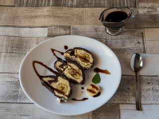 Banana cake with chocolate sauce on a white plate with wooden background