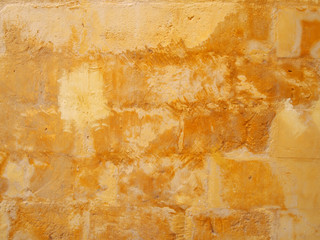an old distressed patched yellow stone wall painted in different shades of faded stained bright...