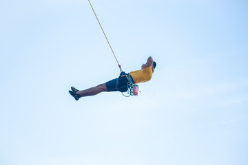 View of man without helmet hanging on a rope while rappelling and shows flying pirouettes in the air  © pablobenii