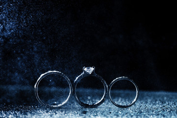 Naklejka na ściany i meble three wedding rings dark background with copy space. Shiny water drops like fog
