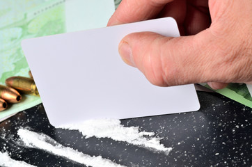 Close-up of man hand making cocaine lines using a white card, gun ammunition in background