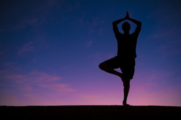 Silhouette of man standing in a yoga pose against colorful sunrise sky