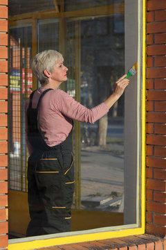 Adult woman paint metal window to yellow color, old shop window renovation