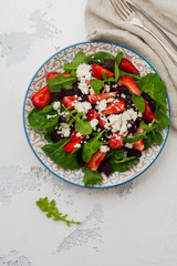 Beets, strawberries, feta cheese and arugula salad in ceramic plate on old concrete table background. Top view.