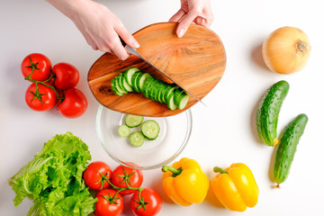Woman cutting fresh cucumber on wooden board ingredients for salad