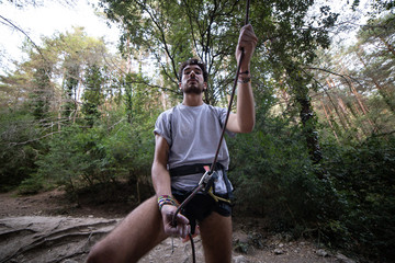 From below of man with rope on rock looking up checking another climber before going up 