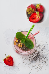 Pink strawberries, banana smoothie with granola and chia seeds in glass on light white concrete background. Top view. Copy space.