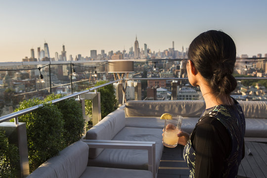 Asian woman drinking a cocktail while watching the sunset over Manhattan, view from Chinatown, Mahattan, New York, USA