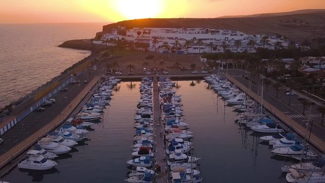 Aerial view of the docks with many yachts during sunset time. Small boats are docked by the coastline on the island of Gran Canaria.