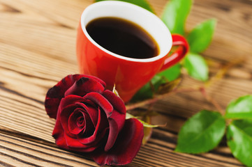 Full cup of black coffee near one red rose on green sprig on old wooden table. Saint Valentine's Day concept