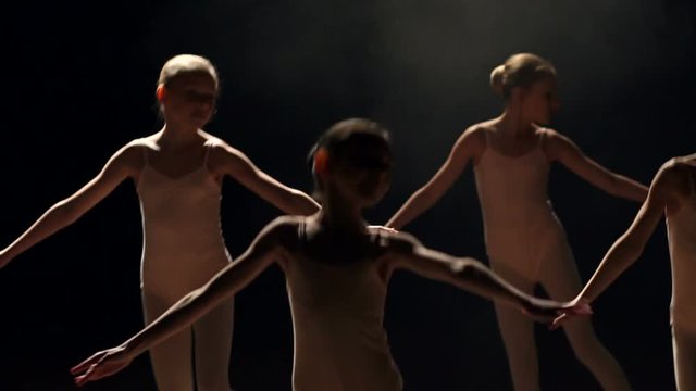 Silhouette of children dancing on stage in the dark. Little cute girls dancing ballet on theater stage on black background in smoke, slow motion.