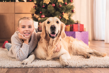 happy kid and golden retriever dog lying near christmas tree with gifts at home