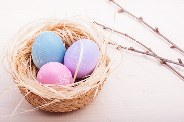 Colored easter eggs in nest on rustic wooden planks with branch