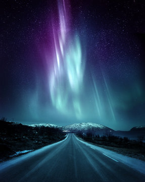 A quite road in Norway with a spectacular Northern Light Aurora display lighting up the night sky above the mountains. A popular destination within the arctic circle for hunting the Northern Lights.