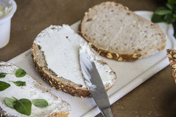  Fresh bread sandwich with soft cheese and herbs on pergamete paper on a stone table. Delicious breakfast sandwich. Culinary background.