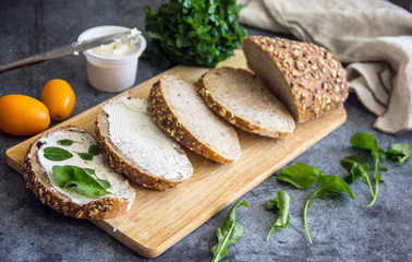 Fresh bread sandwich with soft cheese and herbs on pergamete paper on a stone table. Delicious breakfast sandwich. Culinary background.