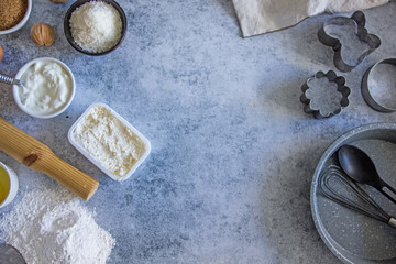 Top view of the ingredients and utensils for making homemade cakes - sugar, flour, sour cream, rolling pin, whisk, baking needles, eggs on a dark stone background. Copy space
