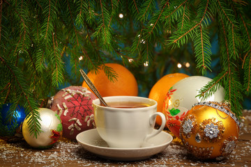 A cup of tea in front,  oranges and New Year toys behind them, fir-tree around this