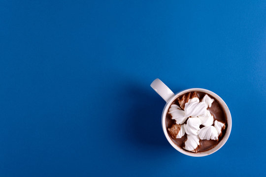 Hot chocolate with marshmallow candies on blue paper background. Top view. Copy space