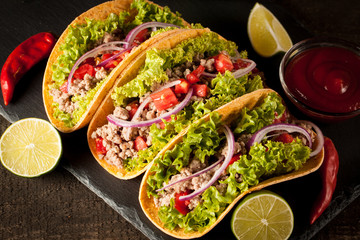 Photo of Mexican tacos with ground meat, beef, beans, onions and salsa on wooden background. Ketchup sauce and lime. A glass o beer in the background.