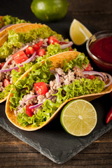 Photo of Mexican tacos with ground meat, beef, beans, onions and salsa on wooden background. Ketchup sauce and lime. A glass o beer in the background.