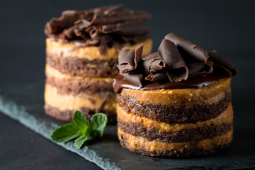 Chocolate cakes on black slatter board with mint, coffee beans on dark background, closeup photo. Fresh, tasty dessert food concept. 