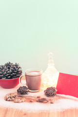 Christmas scene with a cup of hot cocoa, chocolate chip cookies and almonds with red paper for writing / Green Background and wooden table with snow, with text and copy space