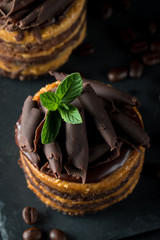 Chocolate cakes on black slatter board with mint, coffee beans on dark background, closeup photo. Fresh, tasty dessert food concept. 