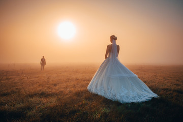 Fototapeta na wymiar Bride in beautiful white wedding dress waiting for groom in magic orange autumn misty morning.