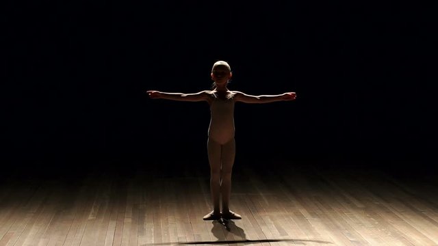 Silhouette of little girl ballerina on stage in darkness, slow motion. A little girl is studying ballet on stage in a choreographic school.