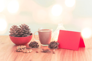 Christmas scene with a cup of hot cocoa, chocolate chip cookies and almonds with red paper for writing / Green Background and wooden table, with text and copy space and bokeh effect