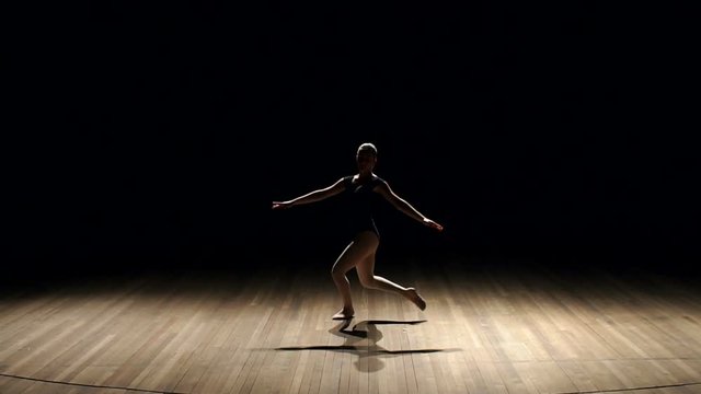 Girl ballerina doing horizontal twine in the air on stage on black background, slow motion.