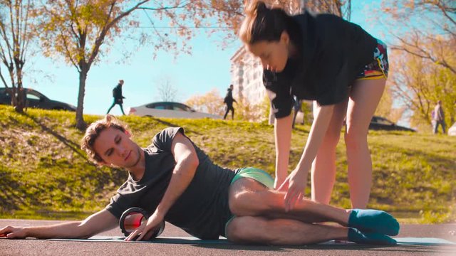 Man doing self massage of the body with a roll. Woman teaching and correcting him. Sunny day, golden autumn