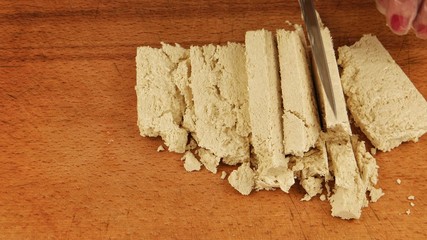 A woman cuts tahini halva into slices on a wooden cutting board