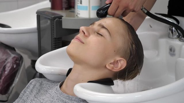 attractive teenager getting his hair washed at the beauty salon by hairstylist, close up