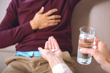 cropped shot of psychotherapist giving glass of water and pill to patient with heartache