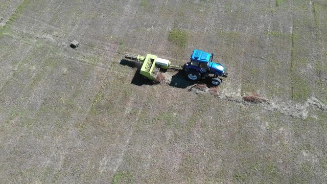 Harvester and tractor in field press grass into bundle, aerial view in Inner Mongolia prairie, China.