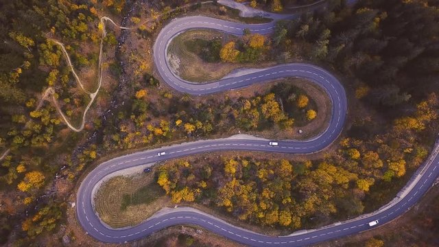 cars driving on serpentine in autumn forest, zoom out by drone, top view