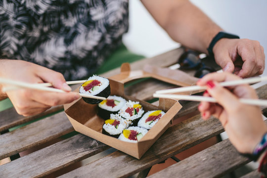 Crop friends eating sushi from box