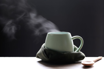 Selective focus of smoke rising with hot soup in cup and spoon on dark background