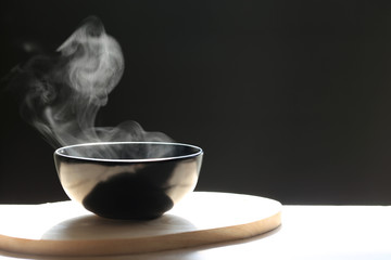 Selective focus of smoke rising with hot soup in cup on dark background