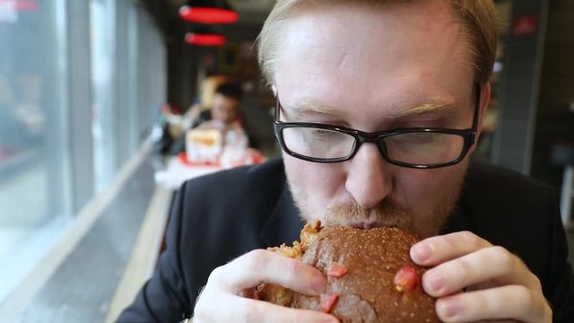 Attractive man with glasses eating Burger in fast food cafe. Slow motion