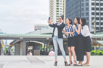 Obraz premium Four happy Asian businesswoman colleague taking selfie with smartphone in city,looking at camera, happy healthy diverse fit people relaxing after working out together in office.