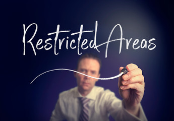 A businessman writing a Restricted Areas concept with a white pen on a clear screen.