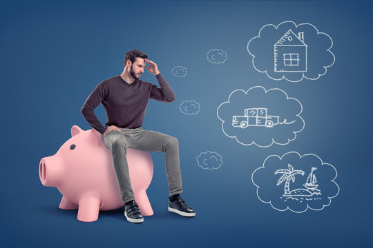 A thoughtful man sits on a large piggy bank near chalk drawings of a house, a car and an island.