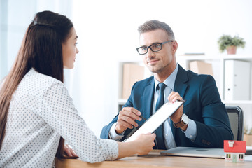 insurance agent pointing at clipboard in clients hand at tabletop in office, house insurance concept