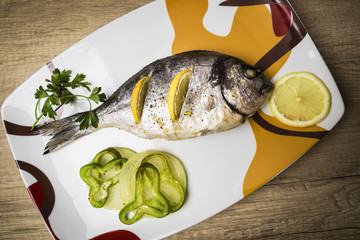 Dorada fish cooked in the oven with lemon, pimento and green onion served on a tray on a wooden table