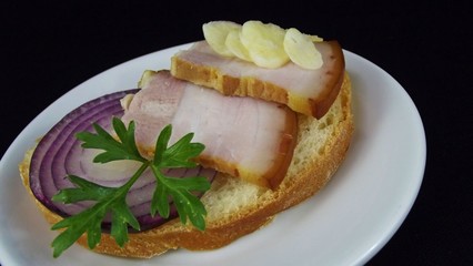 Delicious sandwich with smoked bacon and garlic on a black background.